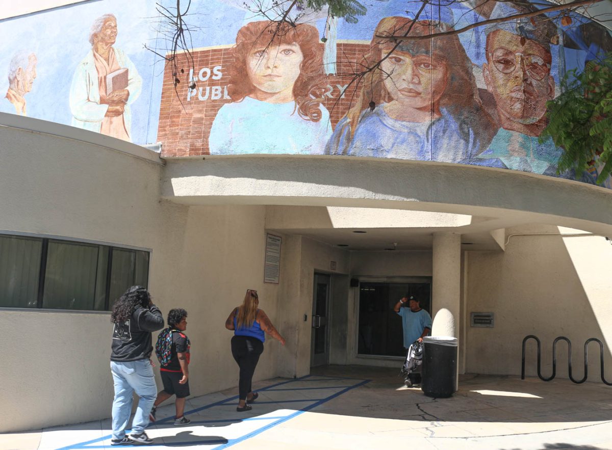 A mother and her two children walk past an unhoused individual as the enter Alma Reaves Woods Watts Branch Library on Tuesday, Aug. 27. (Delfino Camacho | Watts Star)